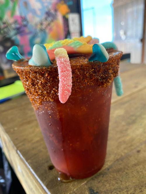 Jarriloko PIFAS en vaso rojo con gomitas y borde sazonado, sobre una mesa. Fotografía original del negocio.